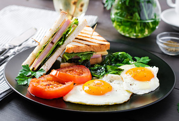 Breakfast: fried egg, spinach, tomatoes and club sandwich on plate.