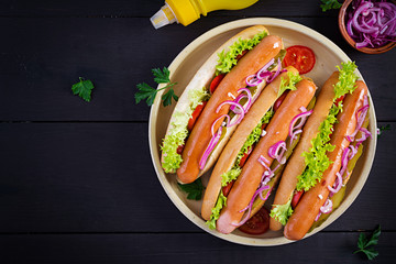 Hot dog with  sausage, pickled cucumber, tomatoes, red onions and lettuce on dark wooden background. Summer hotdog. Top view
