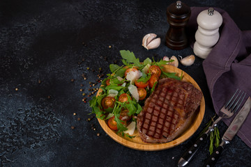 A juicy roast beef steak with fresh salad in a wooden plate stands to the right of the frame on a black concrete background. Horizontal orientation with copy space.