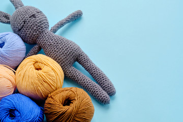 Top view of the bright color yarn clews with grey stuffed amigurumi bunny on the blue background....