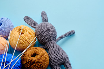 Colorful yarn clews with gray stuffed bunny and needles on the blue background. Concept of amigurumi toy making, handcrafting, knitting, hobby