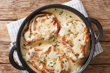 Fried pork chops on the bone served in a creamy cheese sauce with herbs close-up in a pan. Horizontal top view