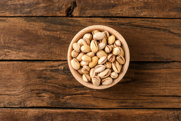 Overhead shot of roasted pistachios in bowl on wooden table. Healthy snacks