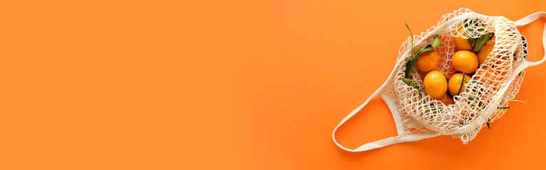 Composition with tangerines in a string bag on an orange background