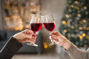 Female hands close up at christmas lights background hold wine glasses
