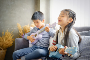 Happy elementary age Asian little kid is smiling  while playing a ukulele during a private music learning lesson at home - 306089347