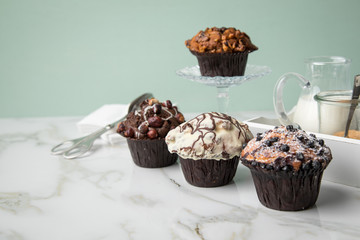 Muffin Auswahl mit Blaubeeren, Walnuss, Haselnuss und Weiße Schokolade mit Milch und Zucker für Kaffeepause auf Marmor Tisch und Grün Hintergrund
