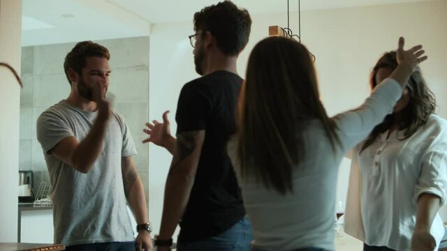 Smiling friends greeting and sitting at table with wine and snacks. Cheerful young people hugging and shaking hands before dinner. Meeting concept