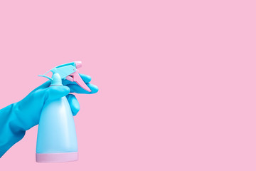 hand in blue rubber glove holding cleaning spray bottle detergent isolated on pink background with...