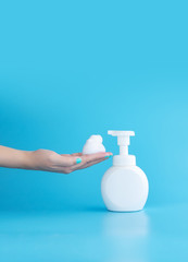 plastic pump bottle and mousse foam or cleansing foam on woman hand isolated on blue background, vertical with copy space. cleaning concept