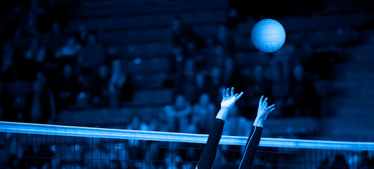 Girl Volleyball player and setter setting the ball for a spiker during a game. Team sport. Blue...