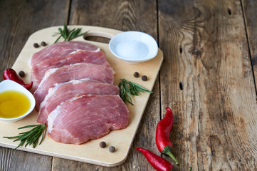 Raw pork with seasonings and oil on a wooden cutting board