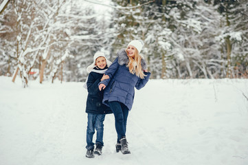 Fototapeta na wymiar Beautiful mother in a blue jacket. Family playing in a winter park. Little boy in a cute hat