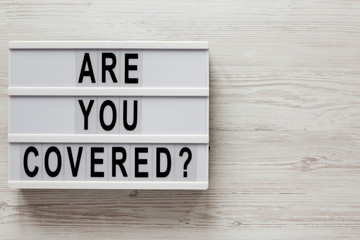'Are you covered?' words on a lightbox on a white wooden background, top view. Overhead, from above, flat lay. Copy space.
