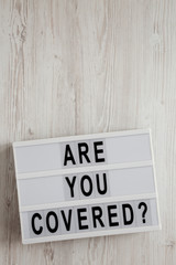 'Are you covered?' words on a modern board on a white wooden background, top view. Overhead, from above, flat lay. Copy space.