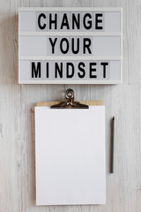 'Change your mindset' words on a modern board, clipboard with blank sheet of paper on a white wooden background, overhead view. Top view, from above, flat lay.