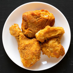 Delicious homemade oven baked fried chicken on a white plate over black surface, top view. Close-up.
