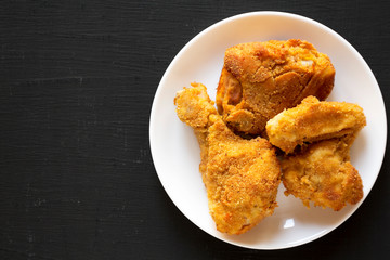Homemade crispy oven baked fried chicken on a white plate over black background, top view. Copy space.