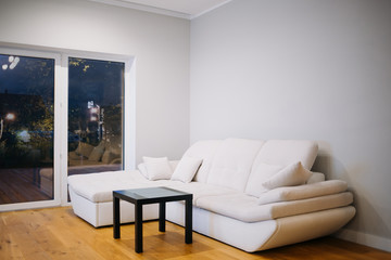 White modern leather sofa against white, empty wall with copy space in simple living room interior
