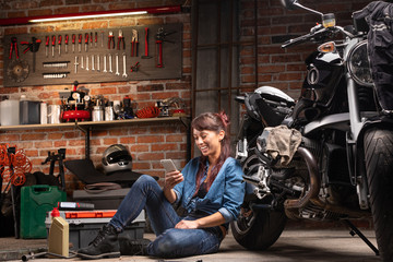Female mechanic relaxing in a motorbike workshop - 306102199