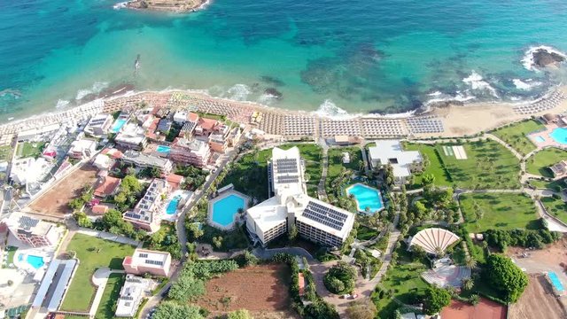 beach world famous as a surfer's paradise. Deck chairs. Ocean surf and waves. Stone cliffs. Aerial view. Greece, Crete, Malia.