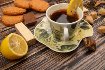 Obraz na płótnie Canvas A Cup of black tea, sliced lemon, brown sugar slices, oatmeal cookies, waffles on a wooden background. Close up.
