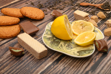 sliced lemon on a saucer, pieces of brown sugar, oatmeal cookies, waffles, pieces of chocolate on a wooden background. Close up.