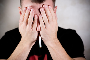 man with a cigarette in his mouth shyly covers his face with his palms