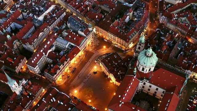 Aerial view malastrana district in Prague at night. Bird eye city square and dome of st. Nicholas church in old town. camera moving from top to bottom on illuminated streets with riding trams 