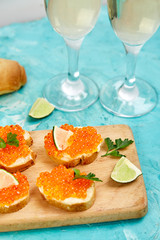 Salmon red caviar in bowl and Sandwiches with on wooden cutting board, glass with champagne on blue background copy space.