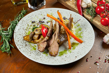 Juicy rack of a young lamb with vegetables and green pasta on a white plate. Restaurant serve from the chef. Wooden background. Close up, selective focus. Food flat lay