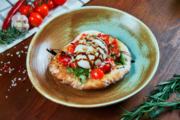 Italian burrata cheese with focaccio served with sauce, tomatoes, basil and nuts. Restaurant dish on a wooden background. Close up view. Food flat lay