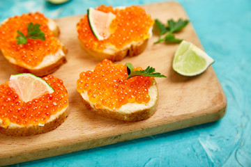 Salmon red caviar in bowl and Sandwiches with on wooden cutting board on blue background copy space. Top view.