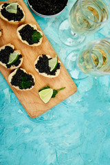 Sandwiches with black caviar. Sturgeon black caviar in wooden bowl, sandwiches and champagne on...