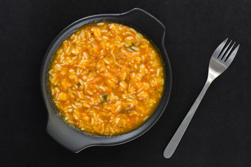 Rice in pumpkin sauce on black plate on black background