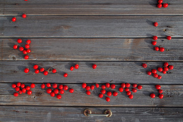 Red sweet hawthorn berries scattered on a smoky wooden background for Christmas greetings or for Valentine's Day.