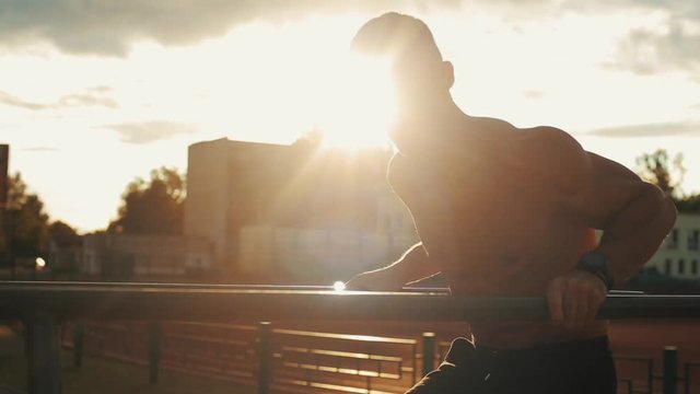 Young sportsman doing dips on parallel bars outdoors with beautiful sunset on the background. Close-up