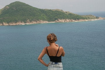 The girl posing on the rock near the ocean in a sunny day