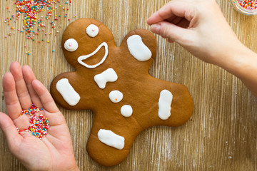 Baked gingerbread cookie man decorated with multicolored balls by woman hand on wooden background