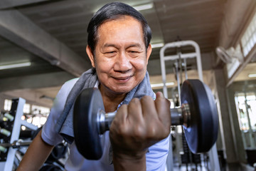 Asian senior man in sportswear training with dumbbell at gym.