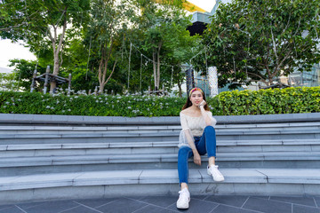 Wide angle portrait of sexy Asian woman sitting on step in the city garden