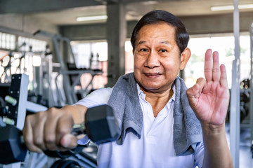 Asian senior man in sportswear training with dumbbell at gym.