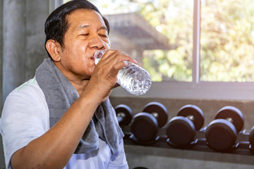Asian senior man in sportswear drinking water at gym.
