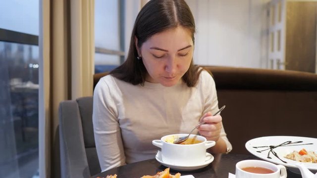 Brunette woman eating vegetable soup in cafe, close-up