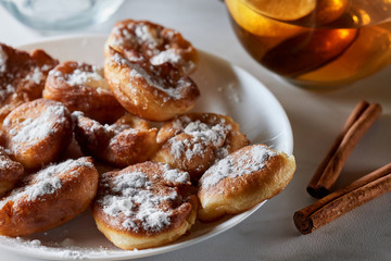 small fried donuts (fritters) with icing sugar on a plate, tea and cinnamon