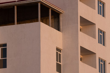 part of the white facade of the building with windows and balconies against a clear blue sky at sunrise and sunset