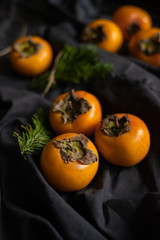 Ripe yellow persimmon with Christmas tree branches on a dark background. New Year's still life