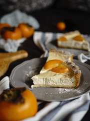 persimmon cheesecake on a dark background. Pieces of cake decorated with persimmons and Christmas tree branches.