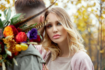 Couple in love walks through autumn forest. Hugs and kisses of men and women, relationships and love. Young couple stands in yellow red grass, a bouquet of flowers in girl hand