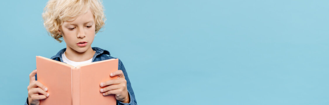 Panoramic Shot Of Blonde And Cute Kid Reading Book Isolated On Blue